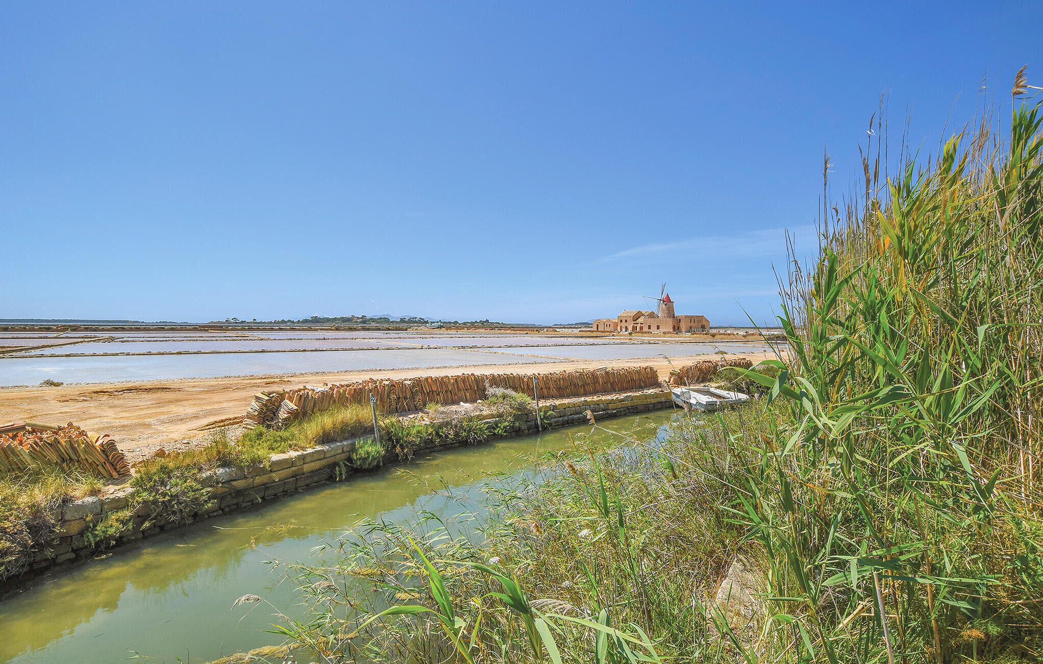 A coastal landscape with a windmill, salt pans, and a small boat.