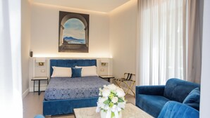 A modern bedroom with a large bed, a blue sofa, a small table with a vase, and a painting on the wall. - B&B L'Infinito 88 Charmant Rooms - Room 2 - Triple De Luxe (Napoli)