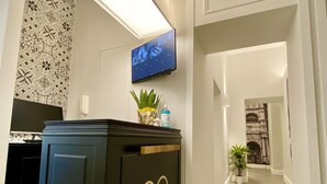 A hallway with a black cabinet featuring a gold emblem, a mounted TV, and a potted plant. - B&B L'Infinito 88 Charmant Rooms - Room 2 - Triple De Luxe (Napoli)