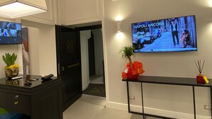 A modern lobby with a reception desk, a television displaying 'NAPOLI ANCORA', and a potted plant. - B&B L'Infinito 88 Charmant Rooms - Room 2 - Triple De Luxe (Napoli)