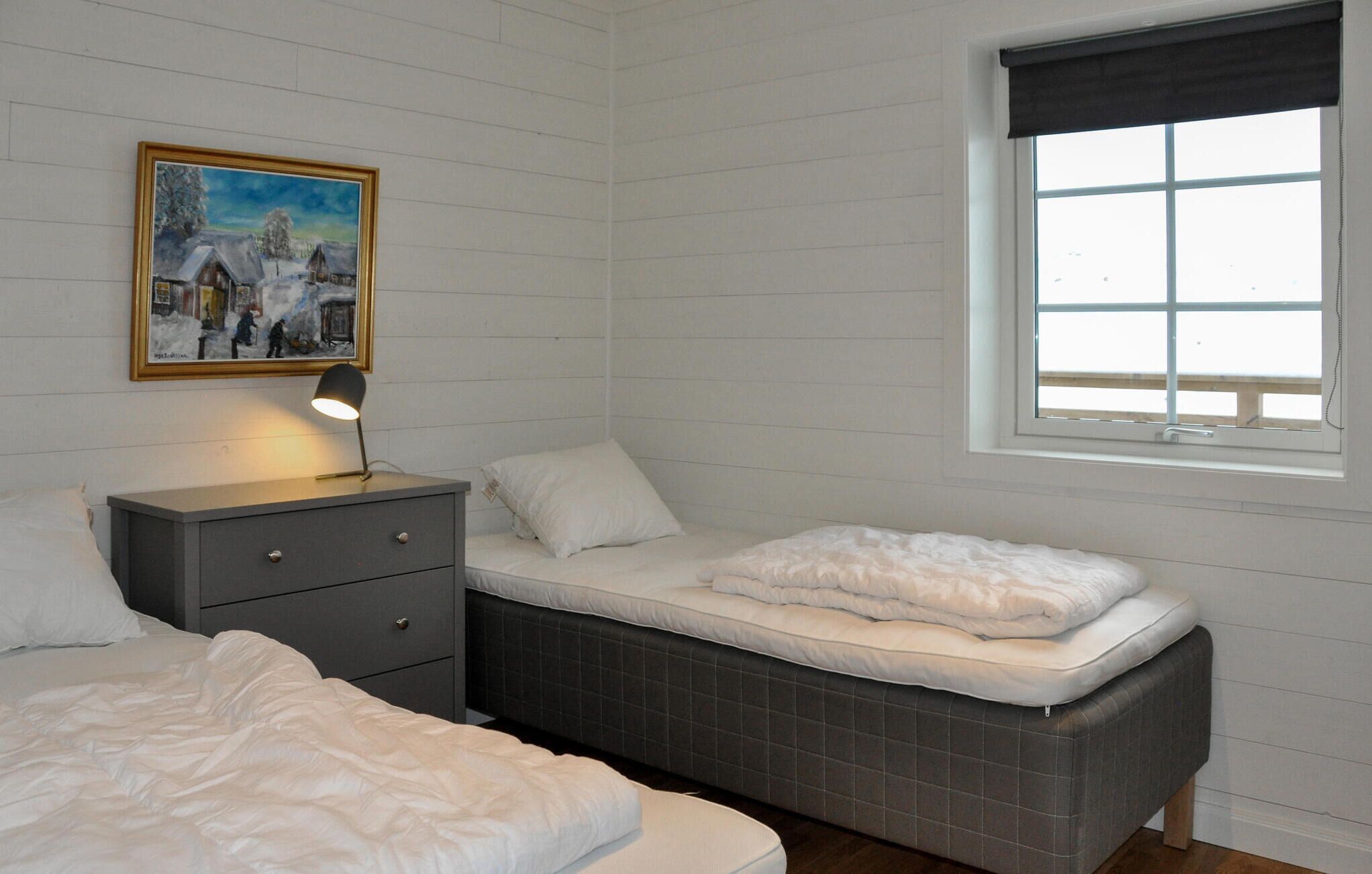 Une chambre à coucher avec un lit, une table de chevet avec une lampe, une fenêtre et un tableau au mur.