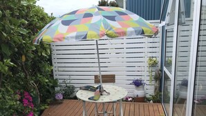 Une terrasse en bois avec une table et des chaises, un parasol coloré et des plantes en pot.