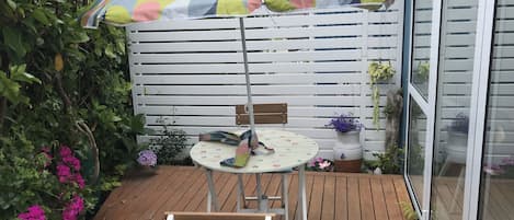 Un pontile in legno con tavolo e sedie, un ombrellone colorato e piante in vaso.