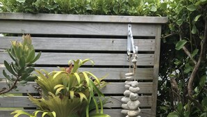 Une jardinière en bois contenant différentes plantes, dont une grande plante à feuilles larges et un cactus, le tout sur fond d’une clôture en bois.