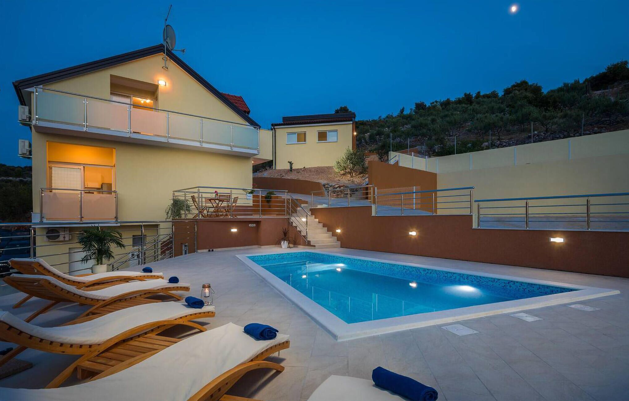 Una casa de dos plantas con piscina, mobiliario exterior y una escalera que lleva a un balcón.