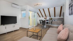 Un salon moderne doté d’un téléviseur à écran plat, d’un canapé agrémenté de coussins décoratifs, d’une table basse et d’un coin repas avec des chaises et une table.