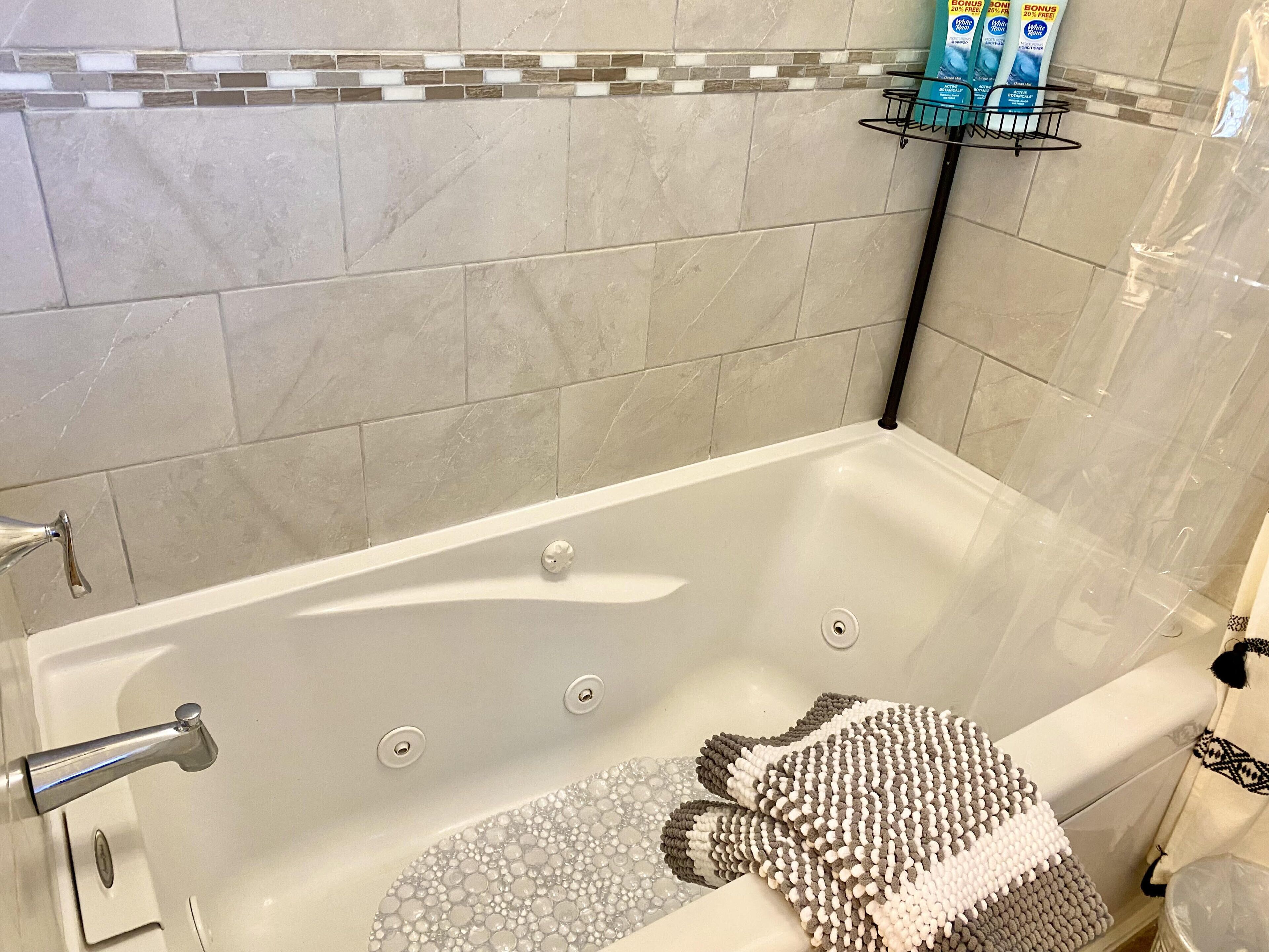 Une salle de bain avec une baignoire, un porte-serviettes avec des articles de toilette et un mur carrelé.