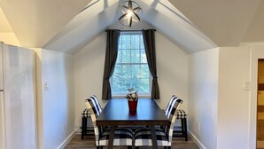 Un coin repas avec une table en bois foncé et des chaises à carreaux, une fenêtre avec des rideaux et un luminaire au plafond.