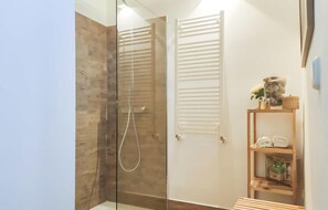 Une salle de bain moderne avec une douche à parois de verre, un plancher en bois et une étagère en bois où sont rangées des serviettes et des articles de toilette.