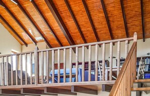 Un balcon en bois, doté d’une balustrade, donne sur une pièce où l’on aperçoit des étagères à livres et un canapé bleu.