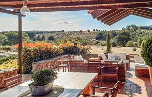 Une terrasse extérieure avec un sol en pierre, des meubles en bois et une vue sur un paysage vallonné parsemé de fleurs orangées.