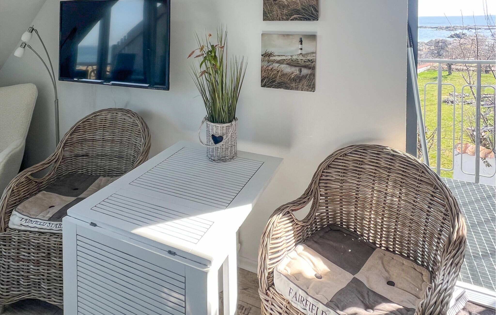 Una habitació amb dues cadires de vimetla, una taula amb un document, un televisor fixat a la paret i quadres amb marc.