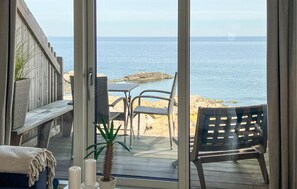 Une terrasse avec vue sur la mer, une chaise, une table et un pot de fleurs.