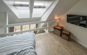 Une chambre avec une lucarne, un lit, une table de chevet avec une lampe et un téléviseur fixé au mur.