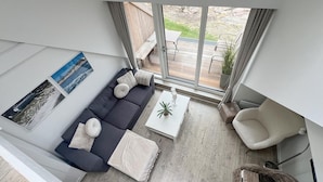 Een moderne woonkamer met een donkere bank, een witte salontafel en een groot raam met uitzicht op de omgeving.