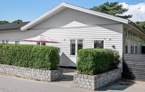 A single-story house with a white exterior, a front porch, and a small patio area with a pink umbrella. - Lovely apartment in Nexø with WiFi (Nexø)