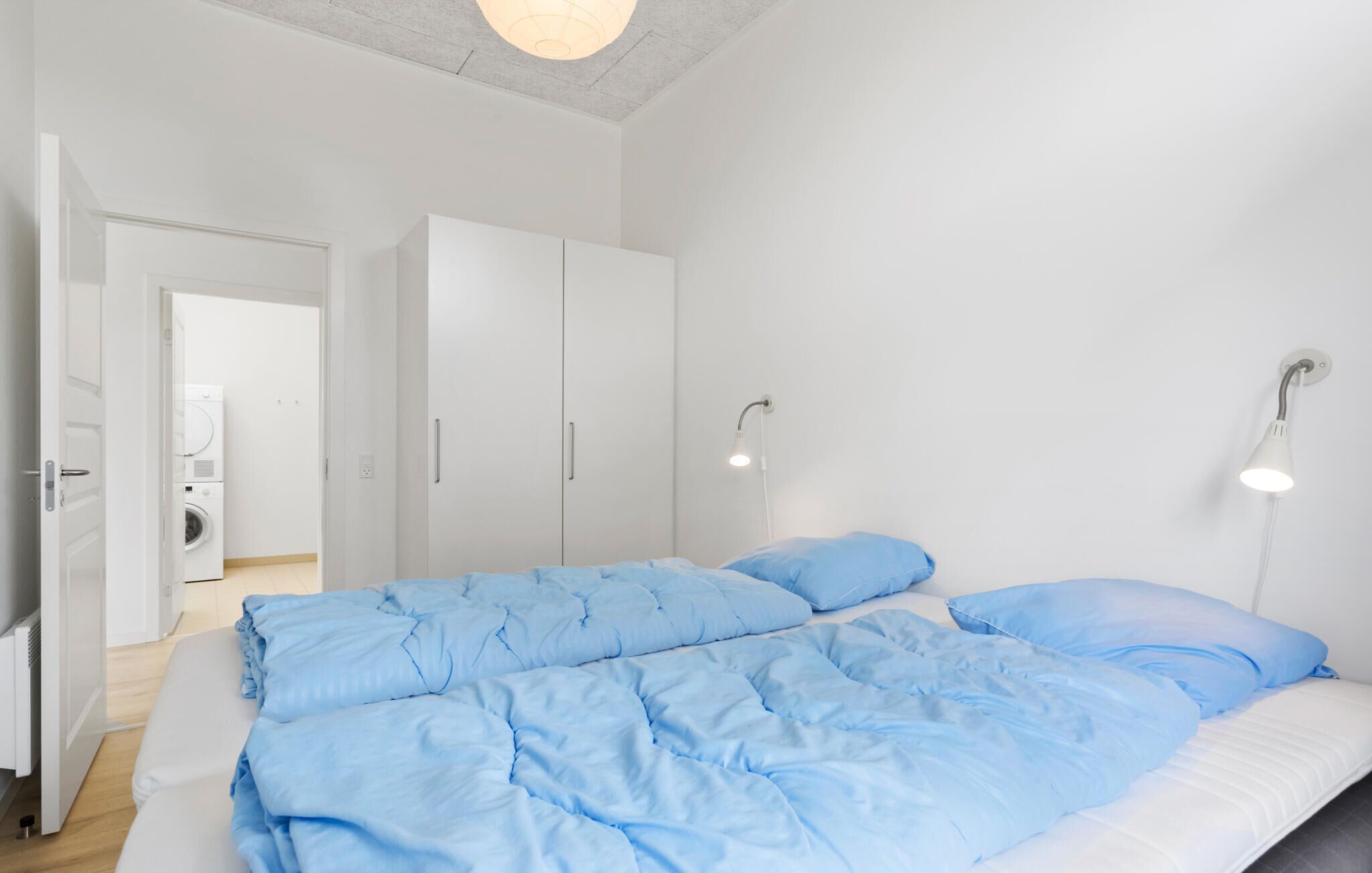 Un dormitorio con cama, armario blanco y lavadora.