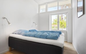 A bedroom with a bed, two bedside lamps, a window with a view of greenery, and a white wall. - Lovely apartment in Nexø with WiFi (Nexø)