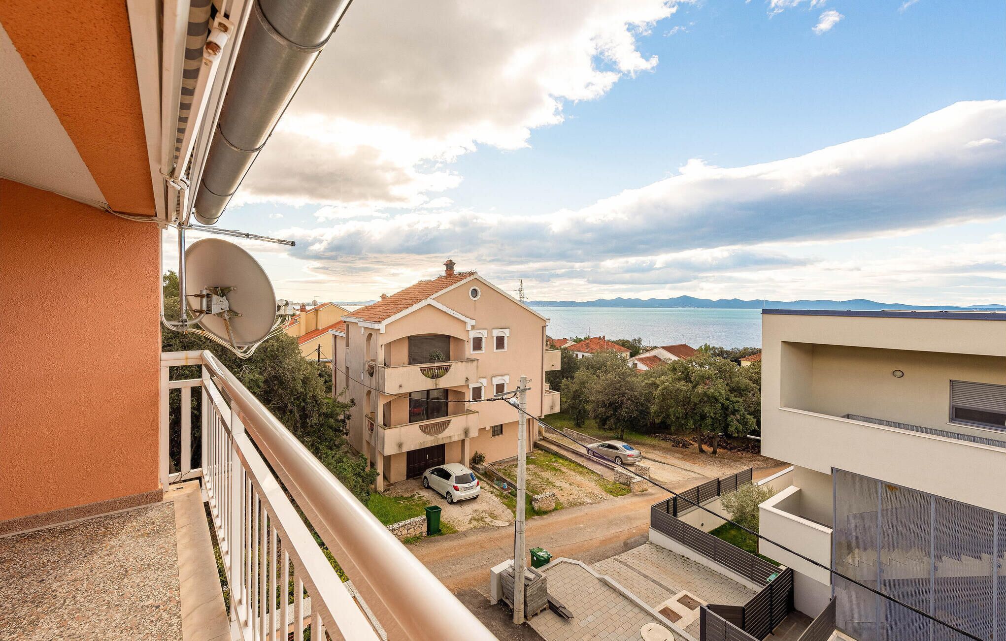 A residential building with a satellite dish, a balcony, and a view of a body of water and mountains in the background.