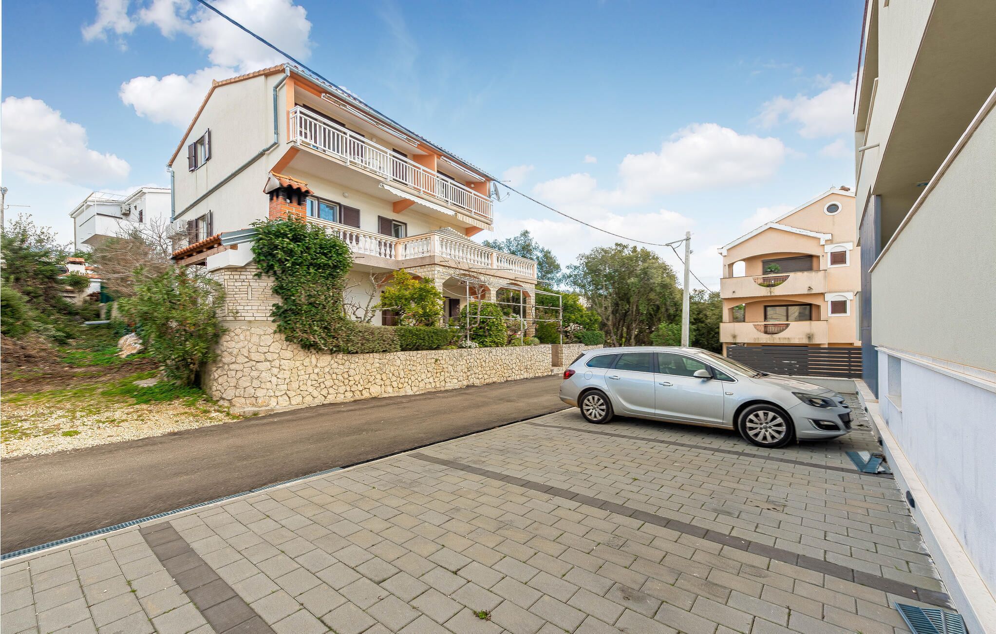 Ein zweistöckiges Haus mit Balkon, einer Steinmauer und einem geparkten Auto.