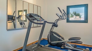 Un gimnasio con cinta de correr, elíptica y bicicleta estática, un espejo grande y una ventana con vistas a edificios.