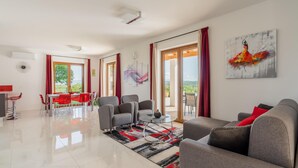 A modern living room with a dining area, large windows, and a view of greenery. - Lovely home in Vizinada (Vizinada)