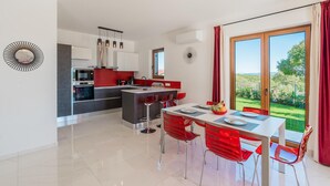 A modern kitchen with a dining area, a large window with a view of greenery, and a red and white color scheme. - Lovely home in Vizinada (Vizinada)