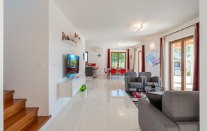 Een moderne woonkamer met een flatscreen-tv, een bank en een eethoek met rode stoelen.