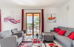 Een moderne woonkamer met grijze banken, een glazen salontafel en rode kussens.