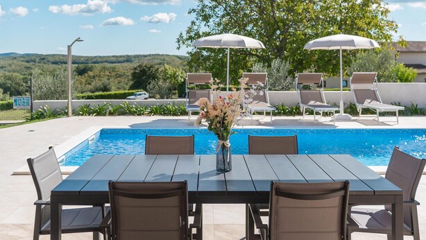 A poolside area with a table and chairs, umbrellas, and lounge chairs. - Lovely home in Vizinada (Vizinada)