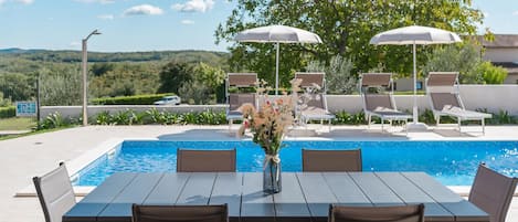 A poolside area with a table and chairs, umbrellas, and lounge chairs.