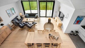 Een moderne, open woonkamer met een eettafel, banken en een groot raam met uitzicht op een houten terras.