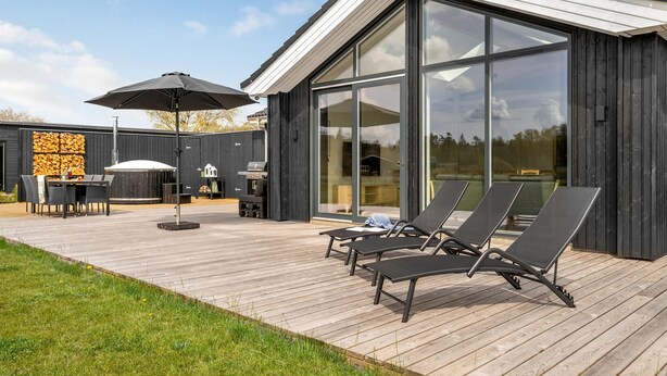 Een modern terras buiten, met een houten vloer, een barbecue en loungestoelen.