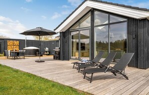 Een modern terras buiten, met een houten vloer, een barbecue en loungestoelen.