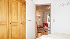 A bedroom with a large wooden wardrobe, a bed, and a view into a living area with a red armchair and a floor lamp. - Awesome apartment in Goslar with WiFi (Goslar)