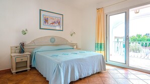 A bedroom with a bed, a nightstand, a wall-mounted lamp, a framed picture, and a view through a sliding glass door. - Amazing apartment in Orosei with WiFi (Orosei)