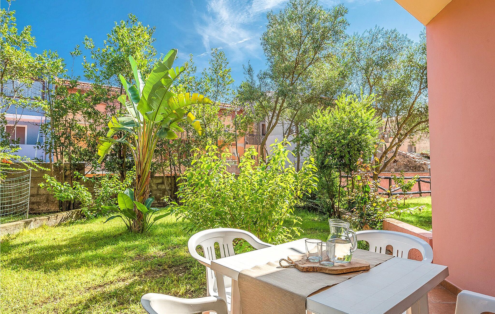 Une terrasse extérieure avec une table et des chaises, entourée d’une végétation luxuriante et d’arbres.