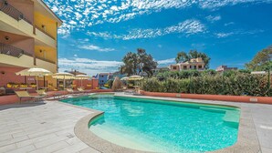 Piscina com espreguiçadeiras e guarda-sóis, cercada por um deck ladrilhado e um muro baixo.