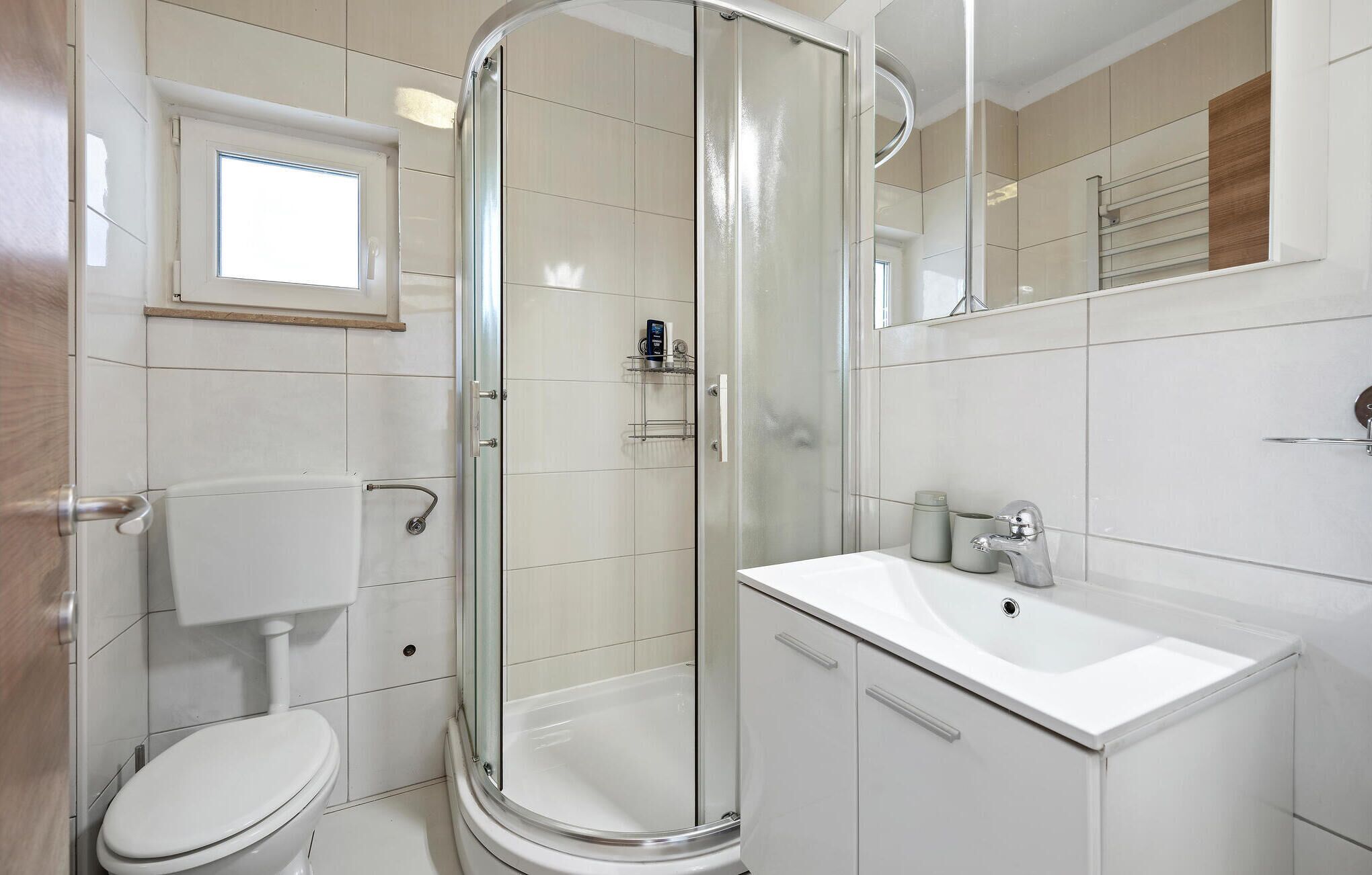 A modern bathroom with a glass-enclosed shower, a white toilet, and a sink with a mirror above it.