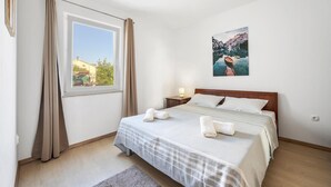 Une chambre à coucher avec un lit, une table de chevet, une fenêtre avec des rideaux et un tableau au mur.