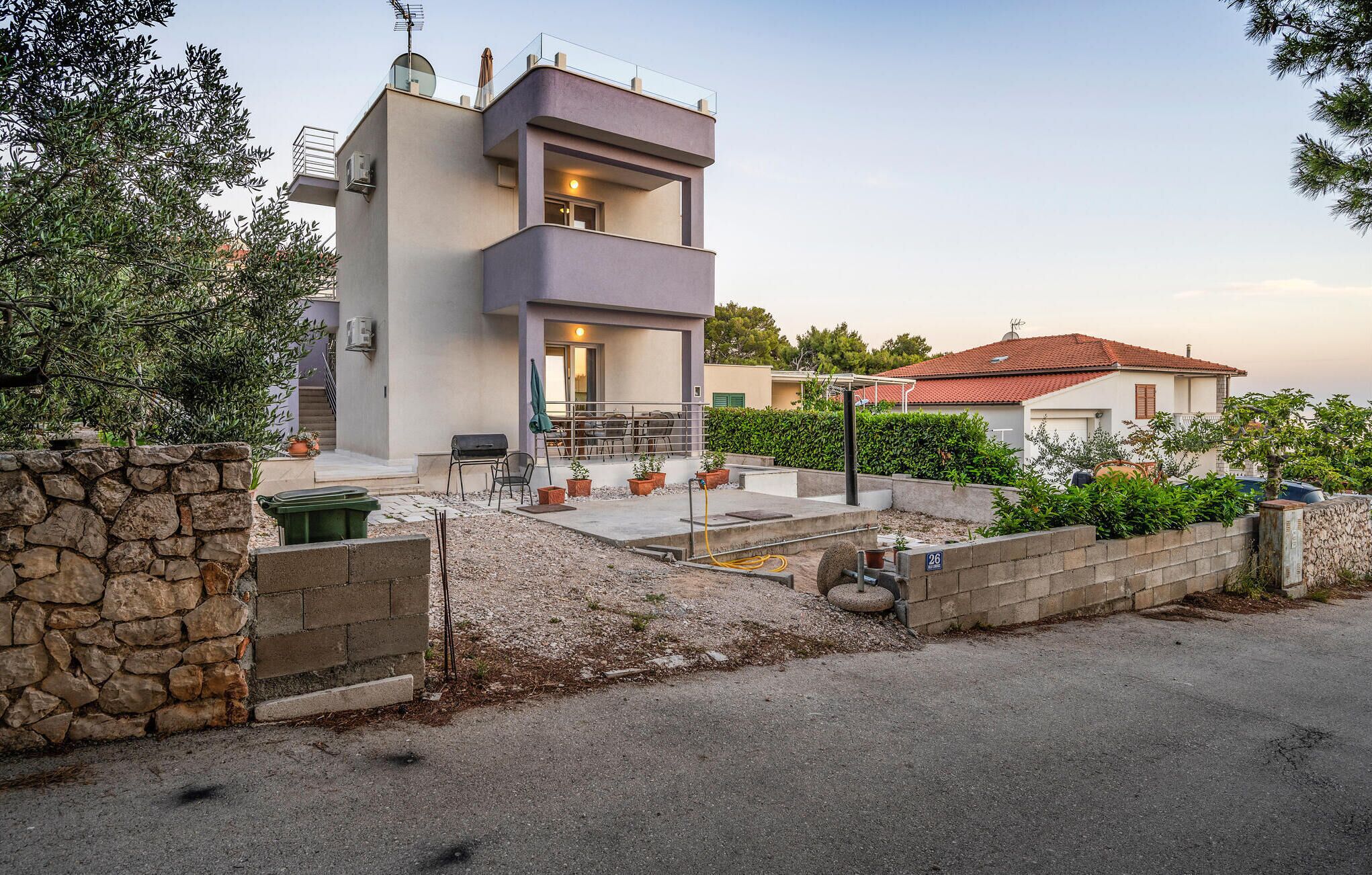 A modern two-story house with a balcony, stone wall, and a paved driveway.