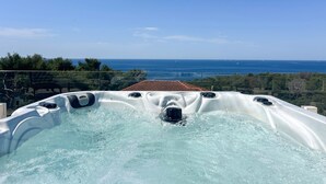 Un bain à remous avec une vue dégagée sur l’océan et un toit recouvert de tuiles en arrière-plan.