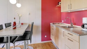 Una cocina moderna con encimera de granito, pileta de acero inoxidable y cafetera. Hay un comedor con una mesa y sillas.