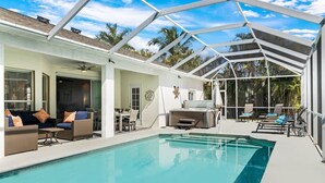 Un área de piscina con terraza cubierta, mobiliario exterior y vistas a palmeras.