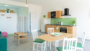 Cocina compacta con comedor, que incluye una mesa de madera, sillas blancas, un refrigerador y un salpicadero de azulejos verdes.