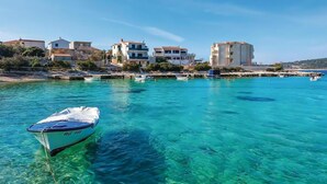 A coastal town with clear turquoise waters, boats docked along the shore, and buildings with balconies overlooking the sea. - 2 bedroom beach front apartment in Rogoznica (Rogoznica)