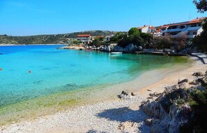 Eine Küstenlandschaft mit klarem, türkisblauem Wasser, einem Kiesstrand und Gebäuden mit roten Dächern.
