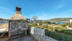 A stone-built outdoor kitchen with a chimney, surrounded by a stone wall and lush greenery. - 2 bedroom beach front apartment in Rogoznica (Rogoznica)