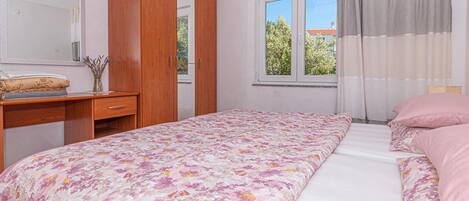 A bedroom with a bed, a wardrobe, a desk, and a window with curtains.