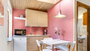 Et lille køkken med mikroovn, kaffemaskine og vask. Der er et spisebord med stole og en vase med blomster.